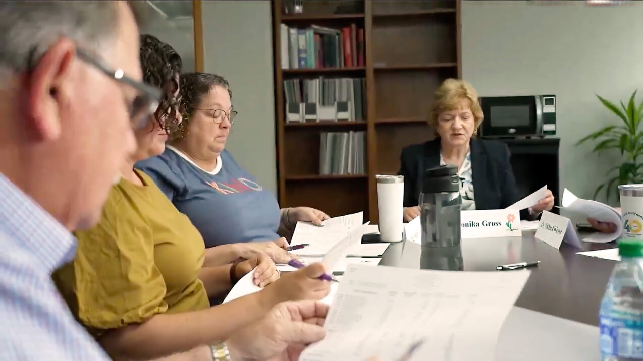 Group of review board members seated at a table, reviewing paperwork together